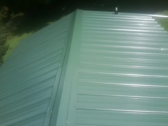 New green metal panels meeting at the ridge of a roof — Flat Roof Repair work by our crew in Dolphin