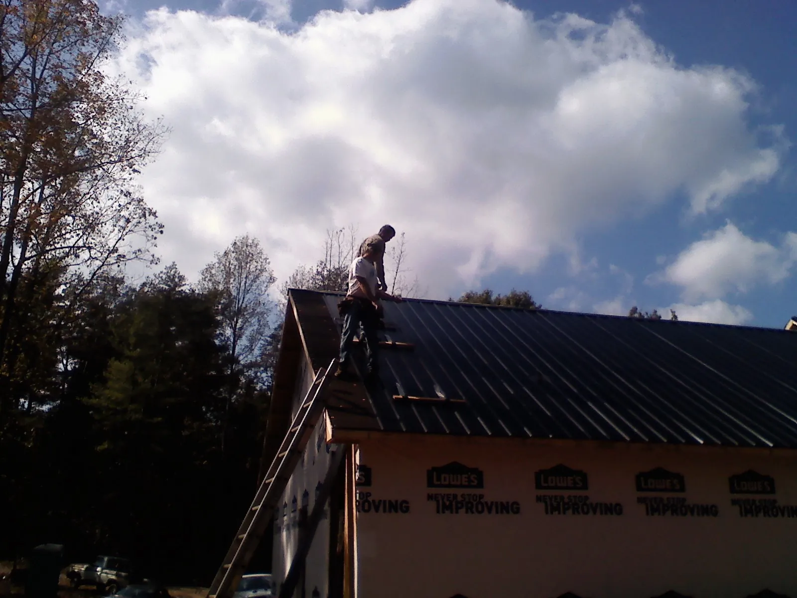 Roofer fastening dark metal panels high against a cloudy sky, from a Roof Inspection job in Dolphin