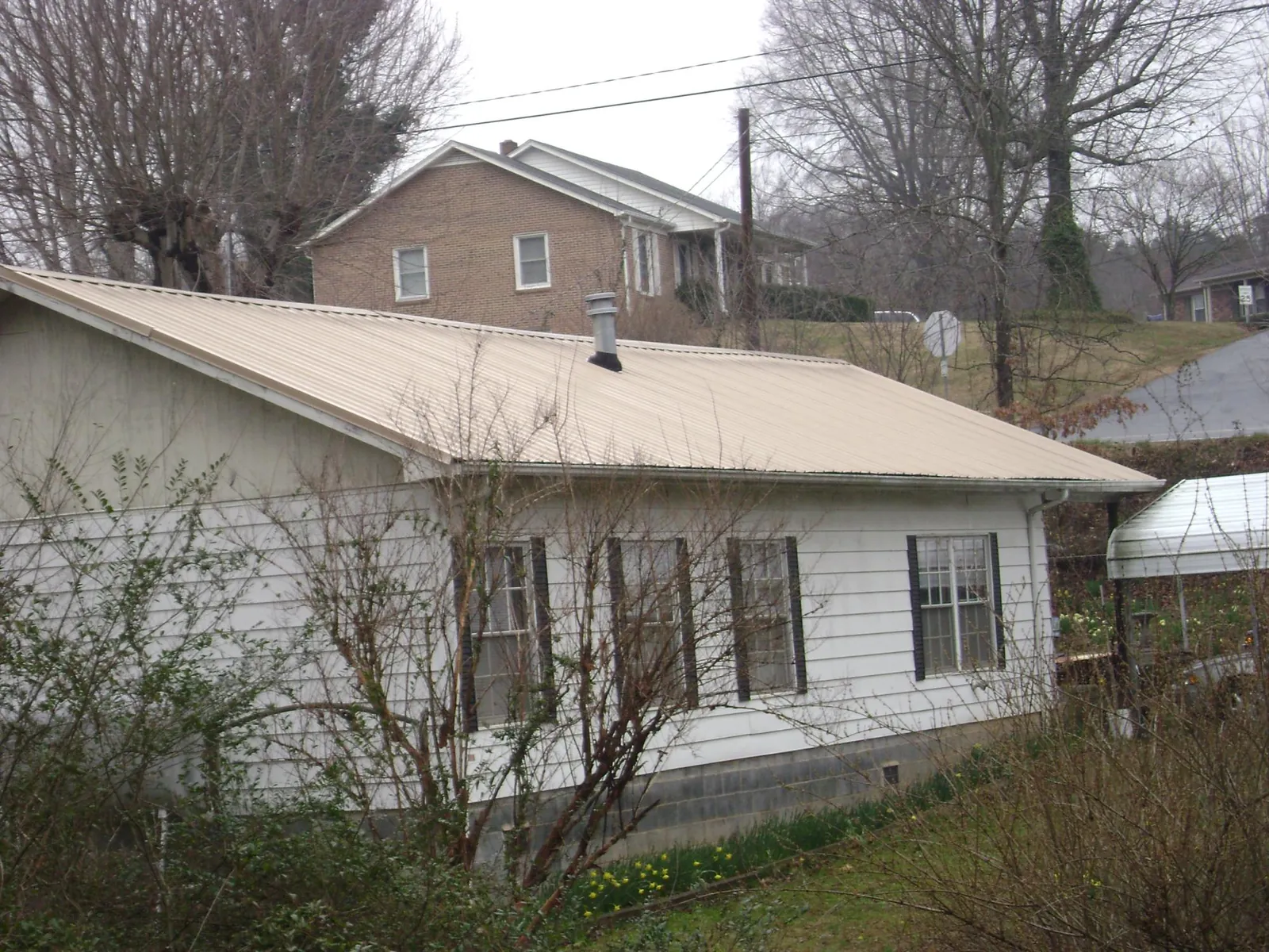 Tan metal roof on a white sided house set into a hillside — Commercial Roofing by Roofing Brothers in Dolphin